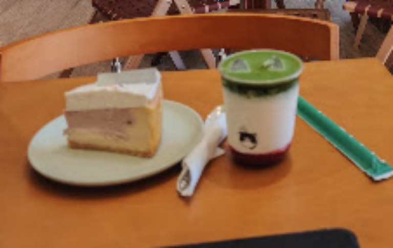Sul tavolo di Chéri: una fetta di torta a strati su un piatto verde chiaro e un matcha in un bicchiere con il cucchiaino verde.