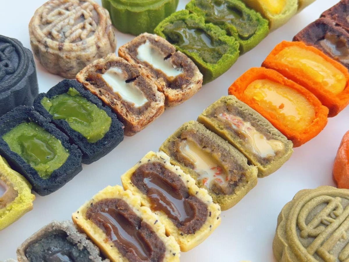 Mooncake tagliati a metà e allineati: ripieni verdi, neri e rossi, e un tuorlo arancione al centro di uno.