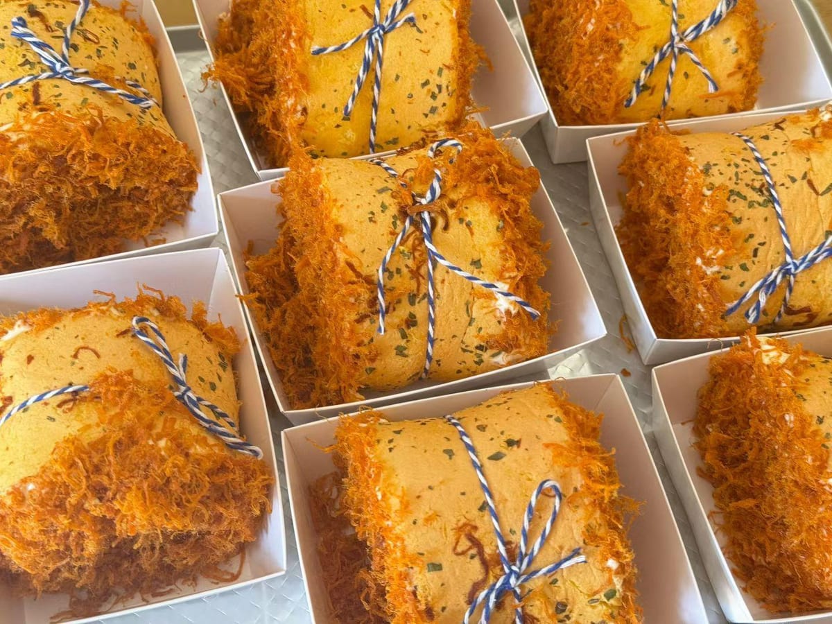 Rotoli di pan di Spagna ricoperti di floss arancione ed erba cipollina, ognuno nella sua scatola bianca, legato con lo spago blu e bianco.