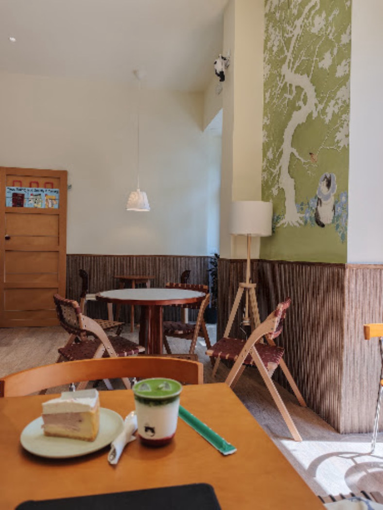 La sala di Chéri: tavoli di legno chiaro, sedie intagliate, la boiserie di listelli scuri e il pannello dipinto sulla parete.